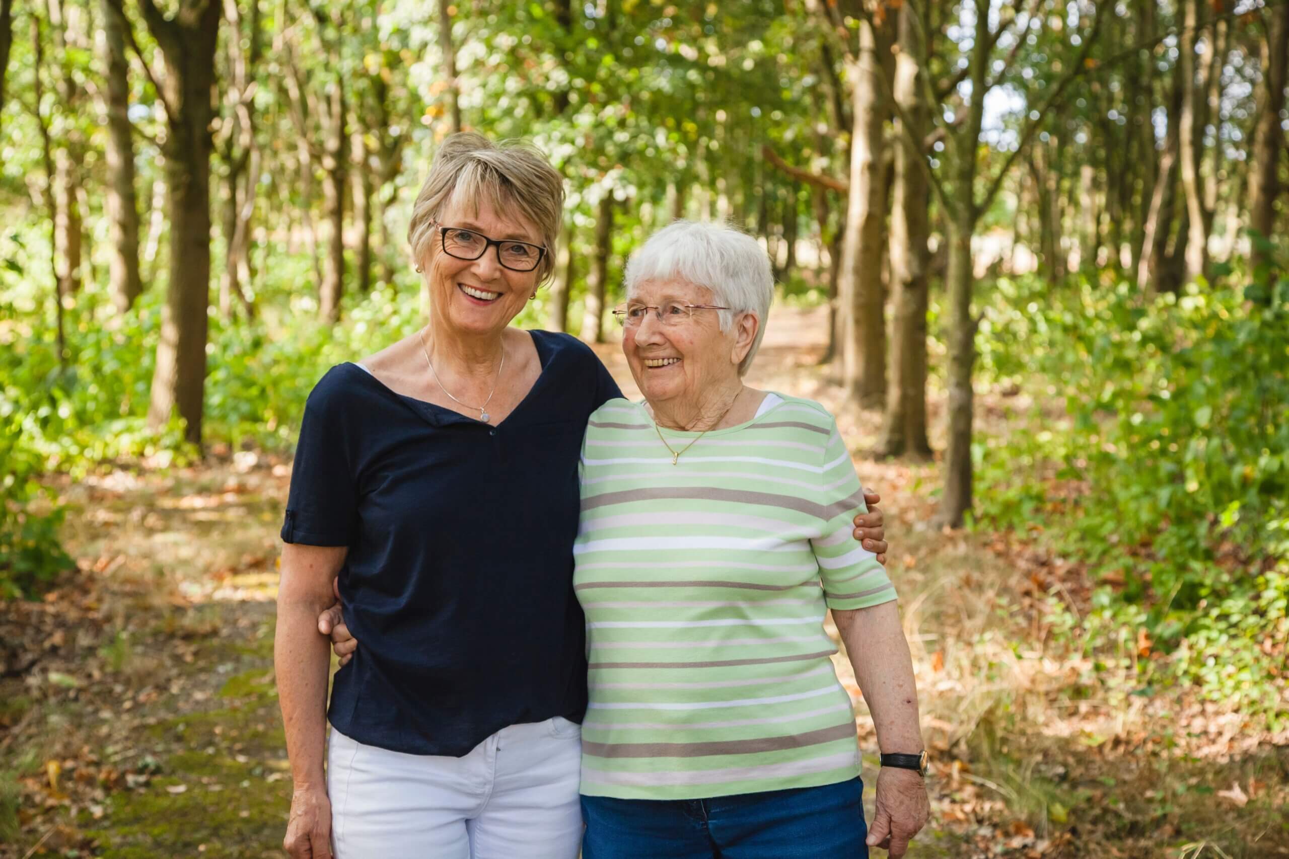 Very old joyful senior lady with her daughter walking embraced in a beautiful park, happy for being together