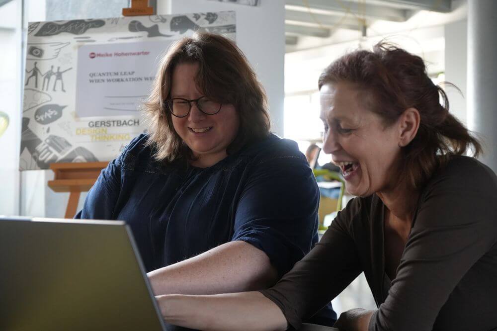 Zwei Teilnehmer:innen lachen bei der Arbeit am Laptop