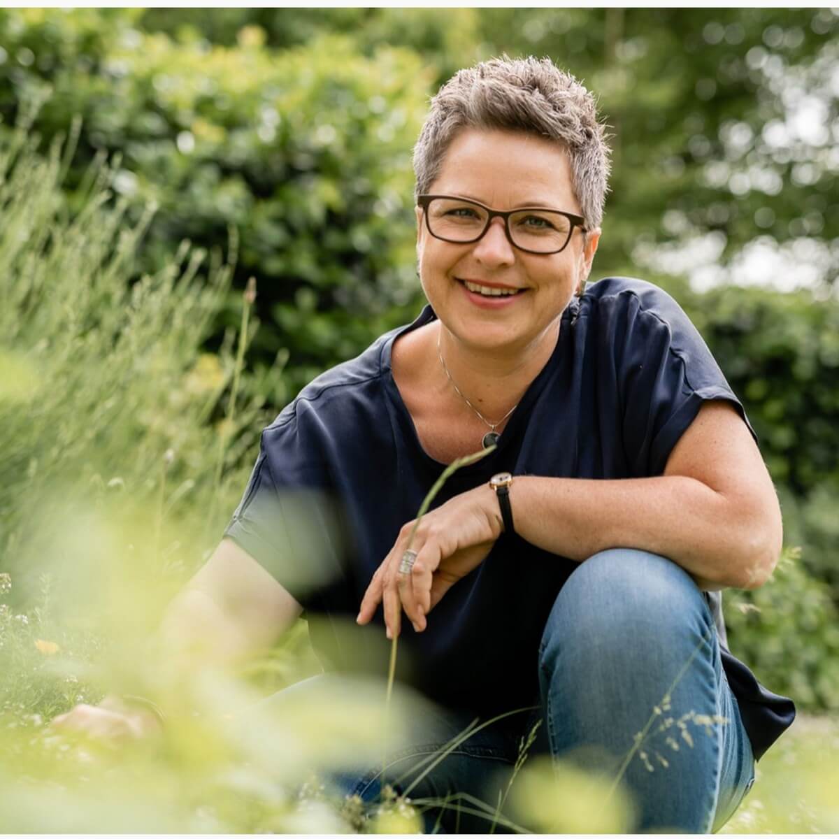 Michaela Hauptmann kniet lachend im hohen Gras