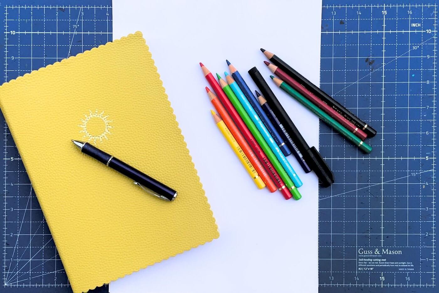 Gelbes Notizbuch, ein Stift und Buntstifte auf einer Schneidematte