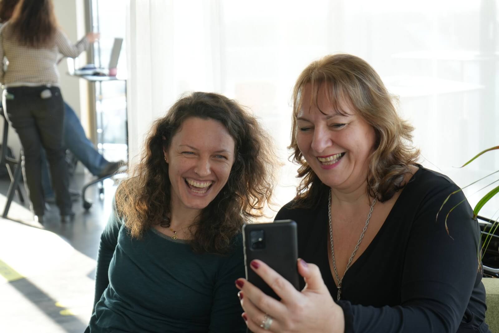 Zwei Teilnehmerinnen lachen gemeinsam über ein Handy auf der Wien Workation